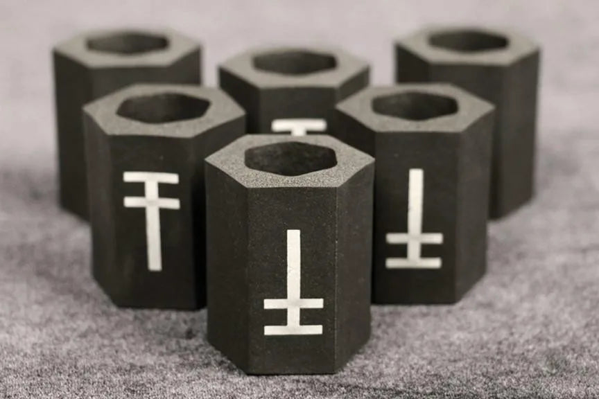A group of black hexagonal memory foam tattoo grip covers with a white symbol on each, arranged on a grey surface.