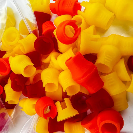 A collection of red and yellow rubber grips for tattooing needles, displayed in an open clear plastic container.