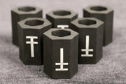 A group of black hexagonal memory foam tattoo grip covers with a white symbol on each, arranged on a grey surface.