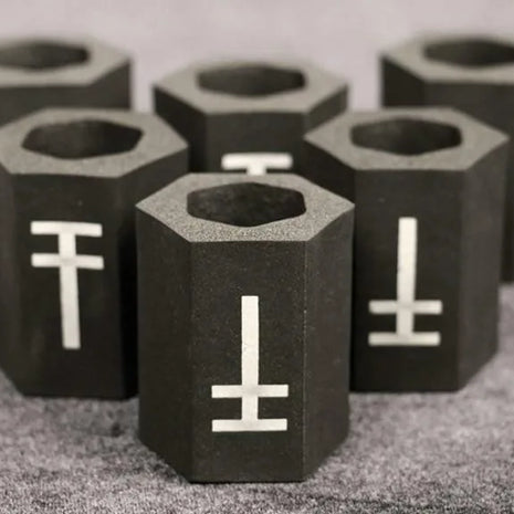A group of black hexagonal memory foam tattoo grip covers with a white symbol on each, arranged on a grey surface.