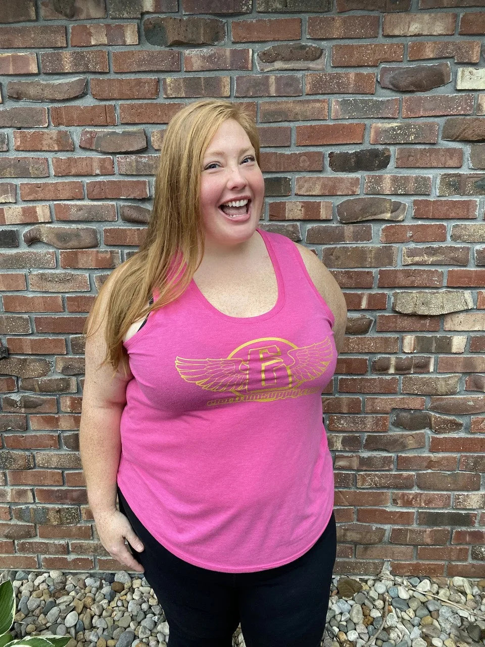 someone wearing a pink electrum tank top with gold lettering 