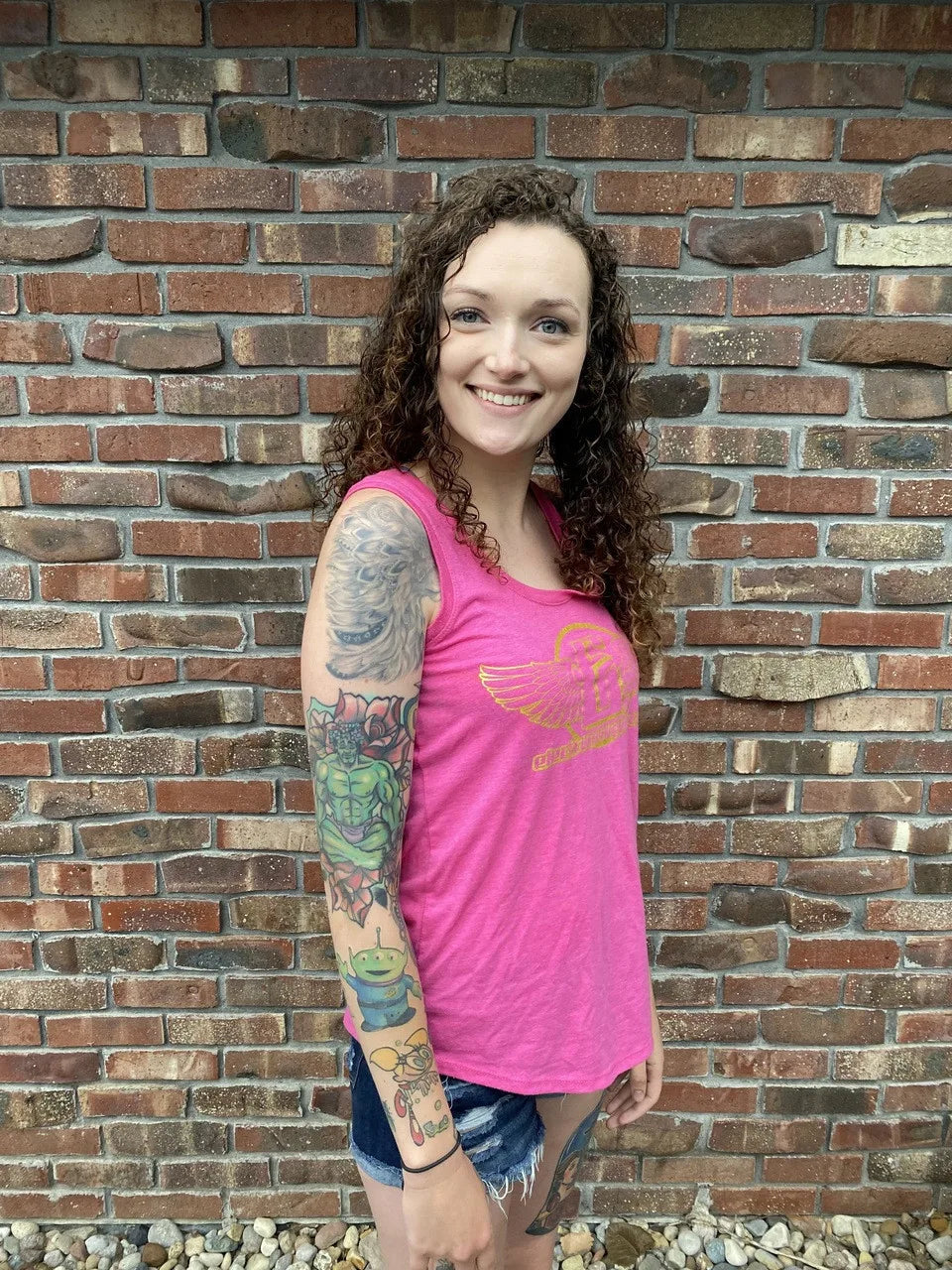 a side profile of a girl wearing a pink tank top with gold electrum flying e logo on front