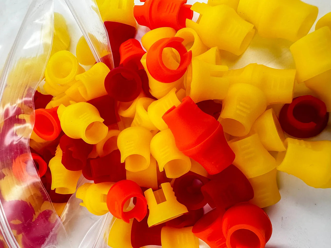 A collection of red and yellow rubber grips for tattooing needles, displayed in an open clear plastic container.